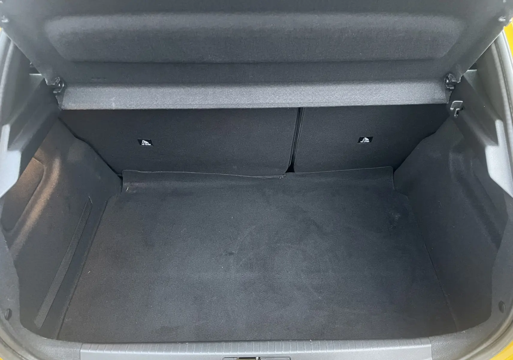 Vue intérieure du coffre spacieux et vide du Peugeot 208 II électrique jaune 2023, avec banquette arrière rabattable.