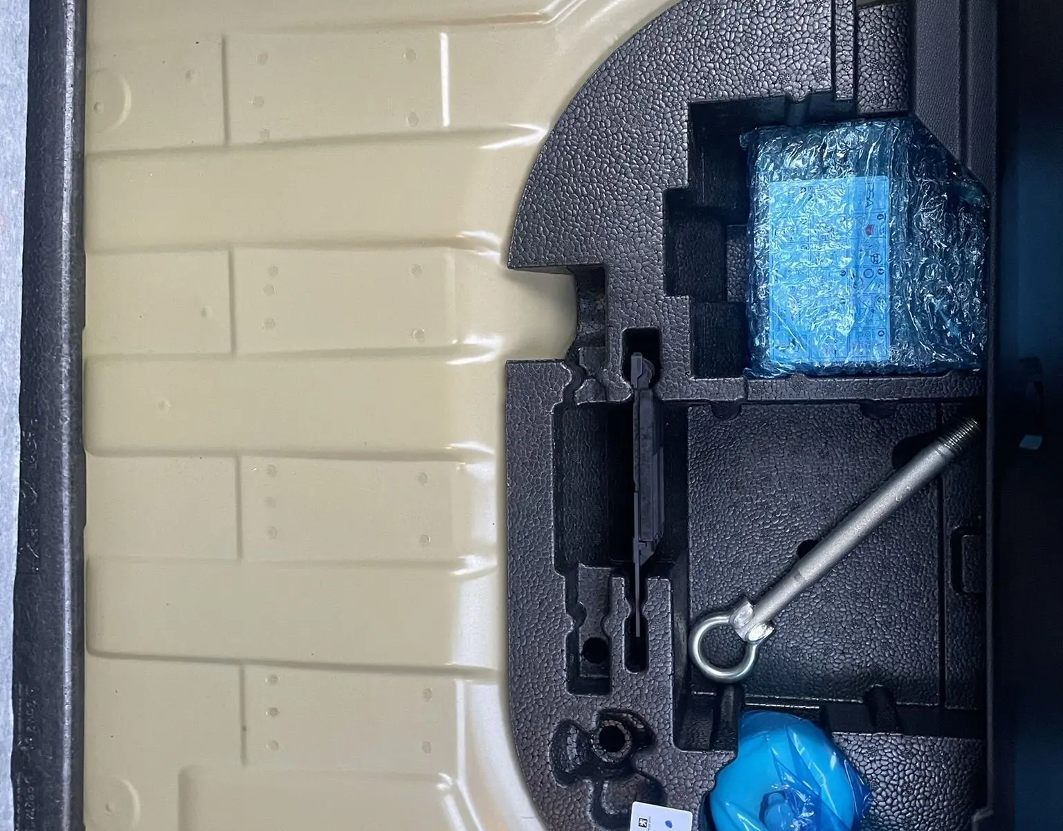 Coffre ouvert d'une Peugeot 208 électrique jaune 2023, montrant le rangement sous plancher avec outils et accessoires emballés.