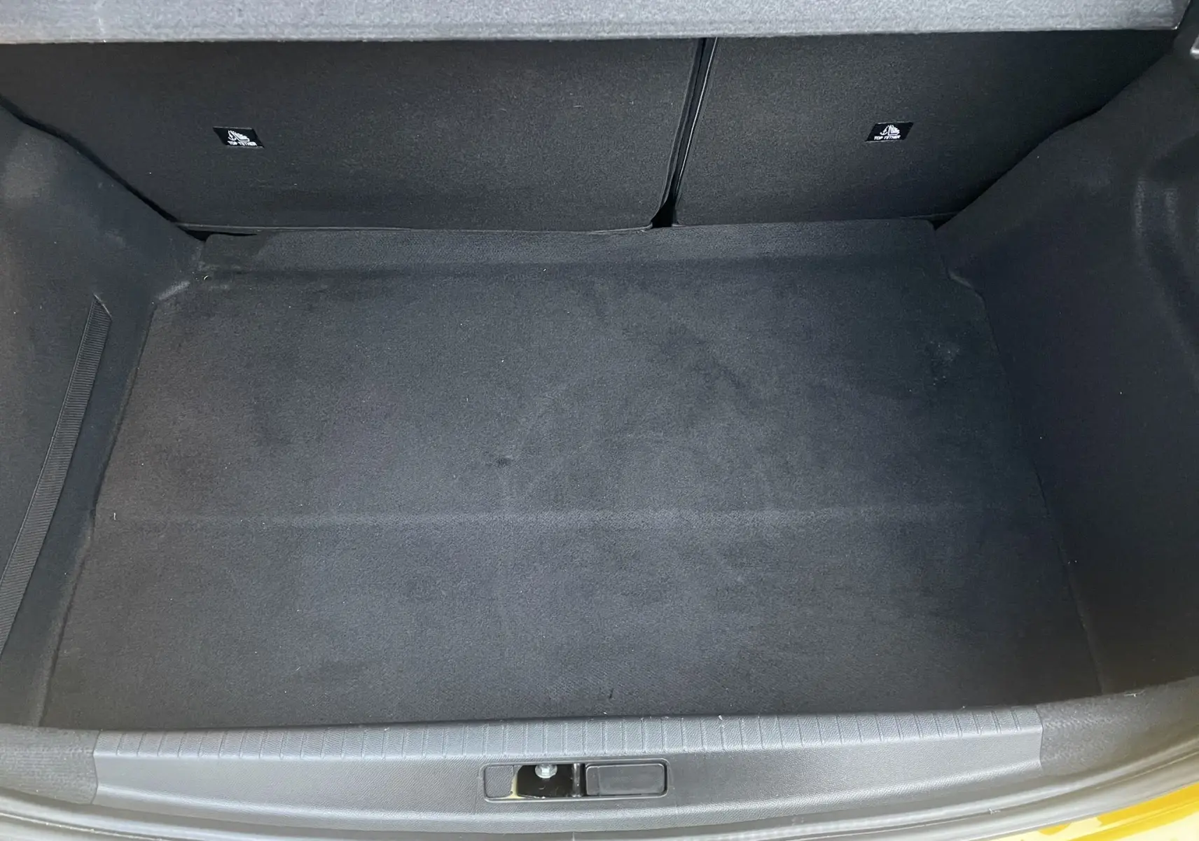 Coffre ouvert vu de dessus d'une Peugeot 208 II électrique jaune 2023, montrant un espace de rangement vide et propre.