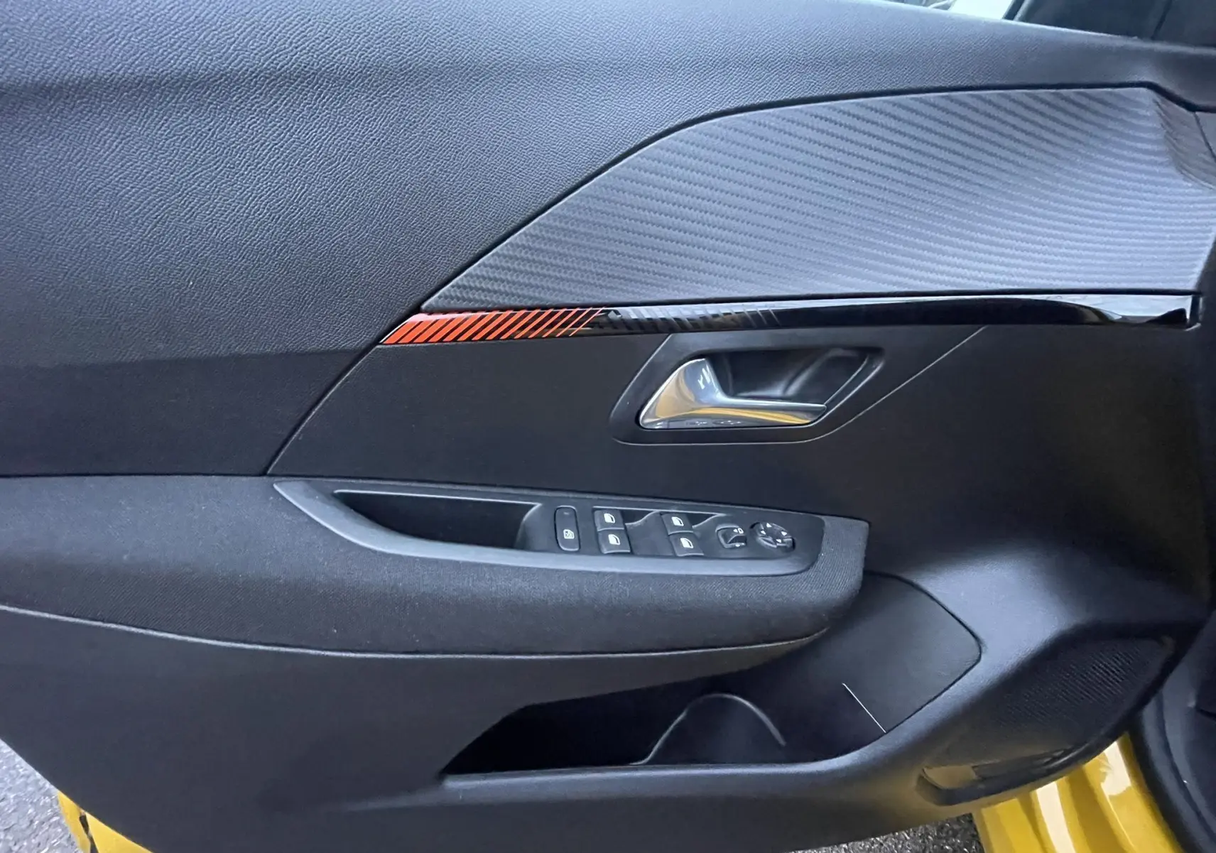 Détail de la porte avant gauche de la Peugeot 208 électrique jaune 2023, avec commandes de vitres et insert décoratif rouge.