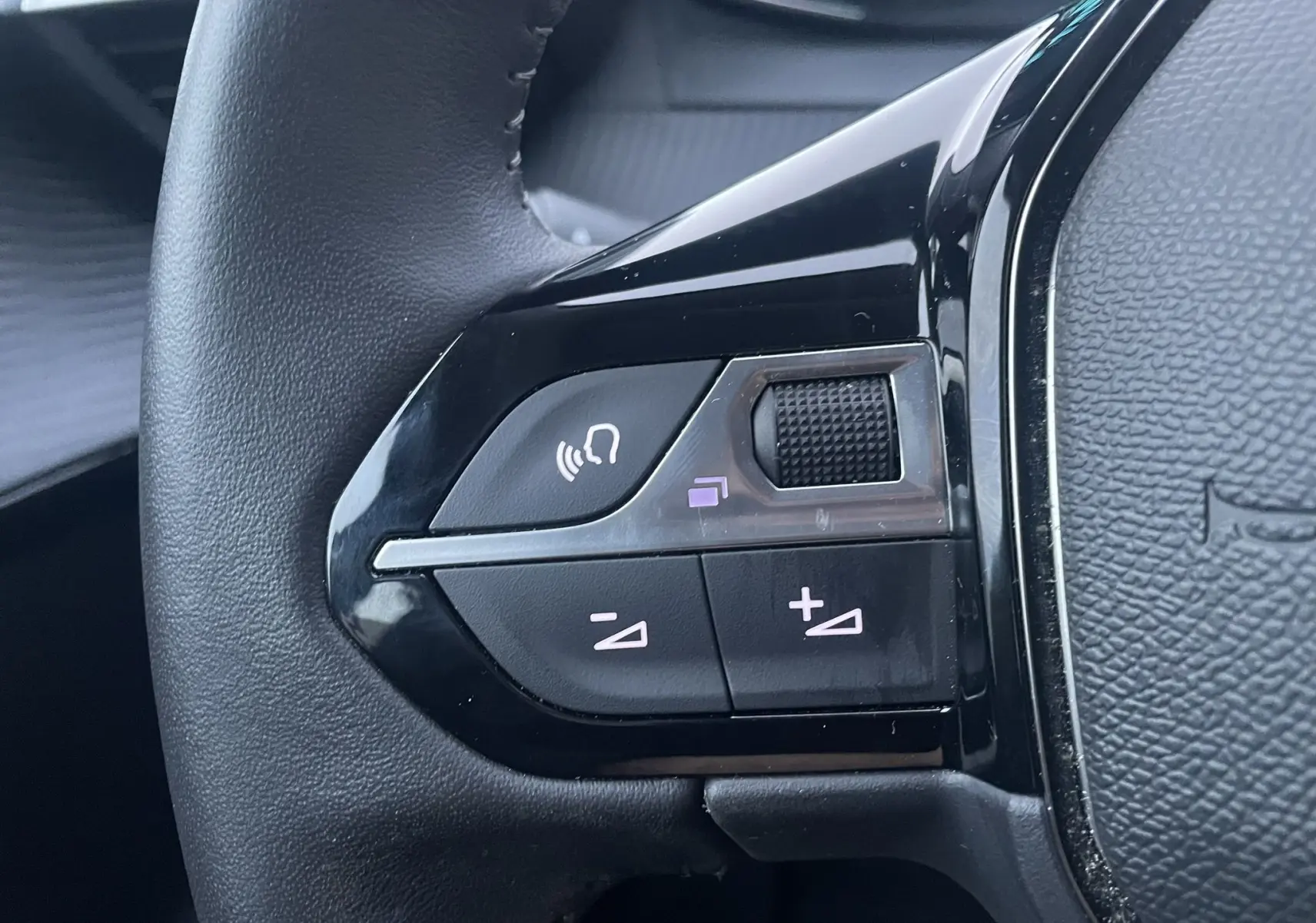 Gros plan sur les commandes gauche du volant noir du Peugeot 208 II électrique jaune, avec boutons de volume et commande vocale.