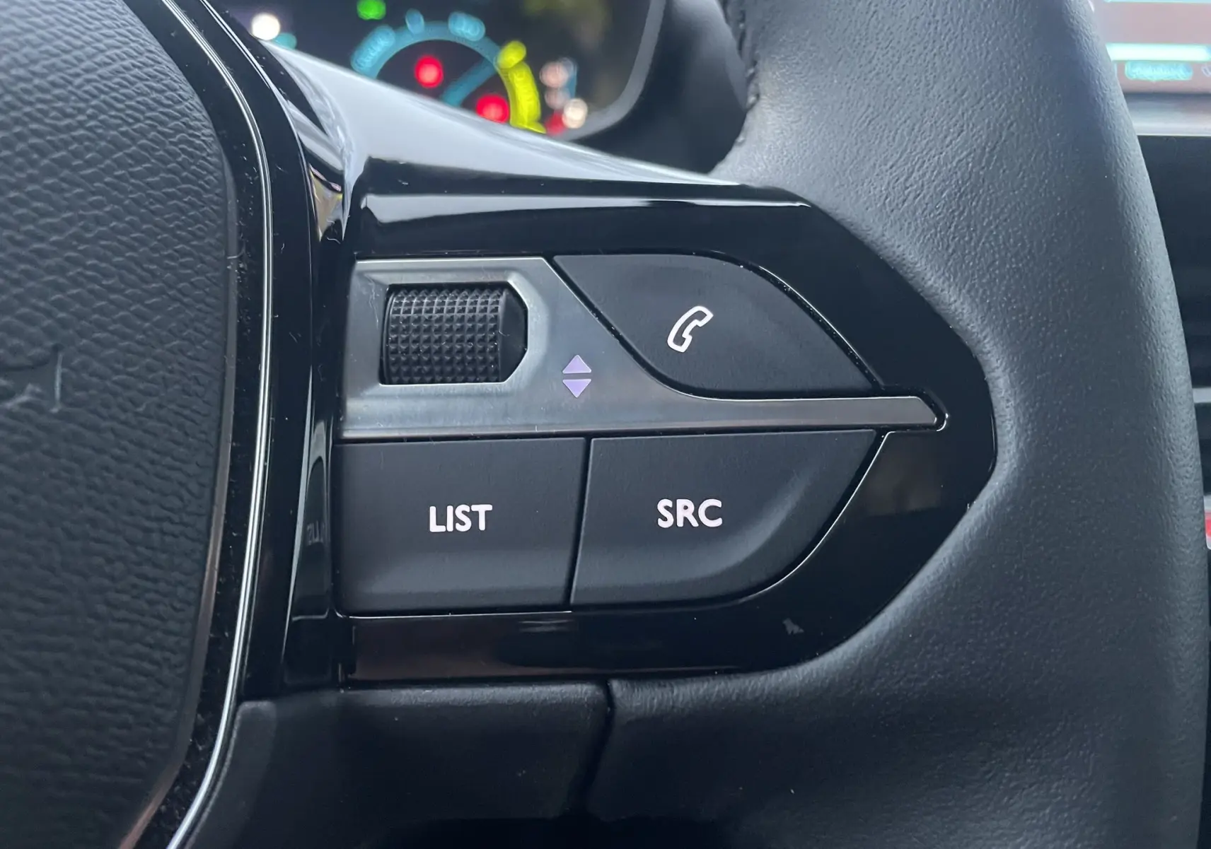 Gros plan sur les commandes gauche du volant noir du Peugeot 208 II électrique 2023, avec boutons LIST et SRC visibles.