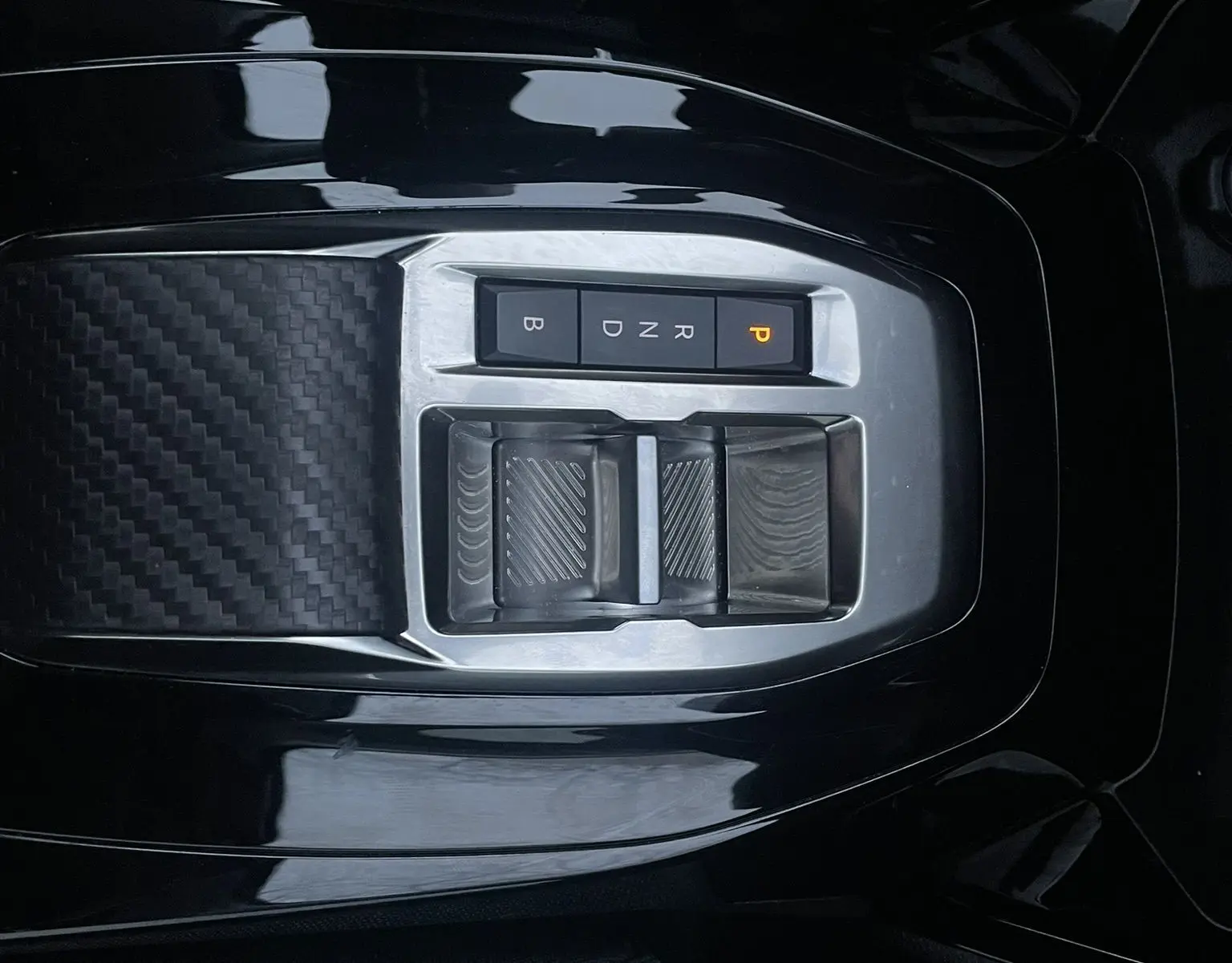 Gros plan sur la console centrale noire de la Peugeot 208 II électrique 2023 avec commandes de boîte automatique et finition carbone.