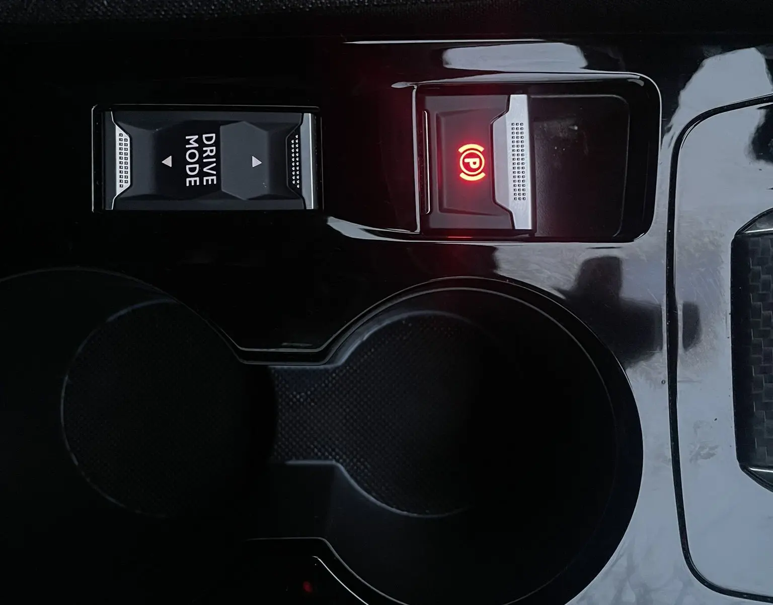 Gros plan sur la console centrale noire du Peugeot 208 électrique 2023, avec bouton Drive Mode et frein à main électronique allumé.