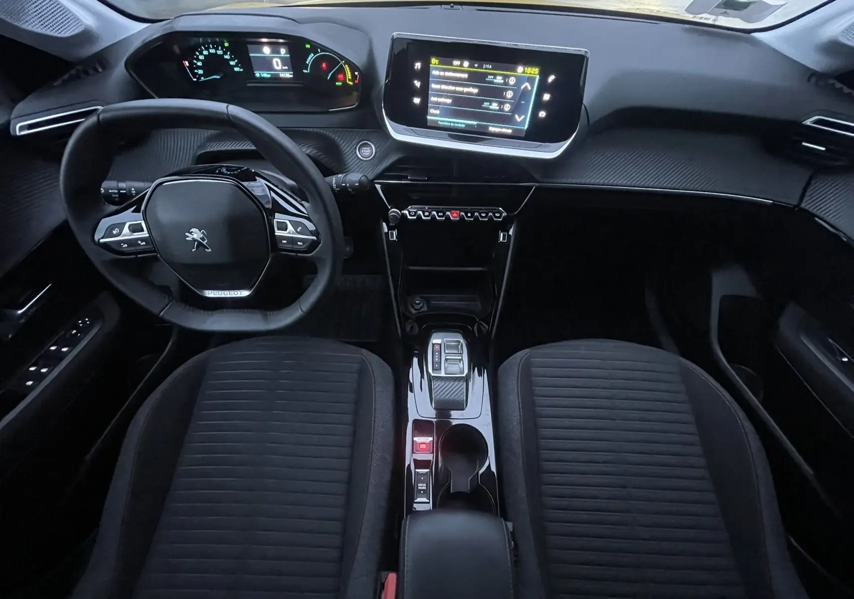 Vue intérieure frontale du tableau de bord et console centrale de la Peugeot 208 II électrique 2023 avec volant compact et écran tactile.