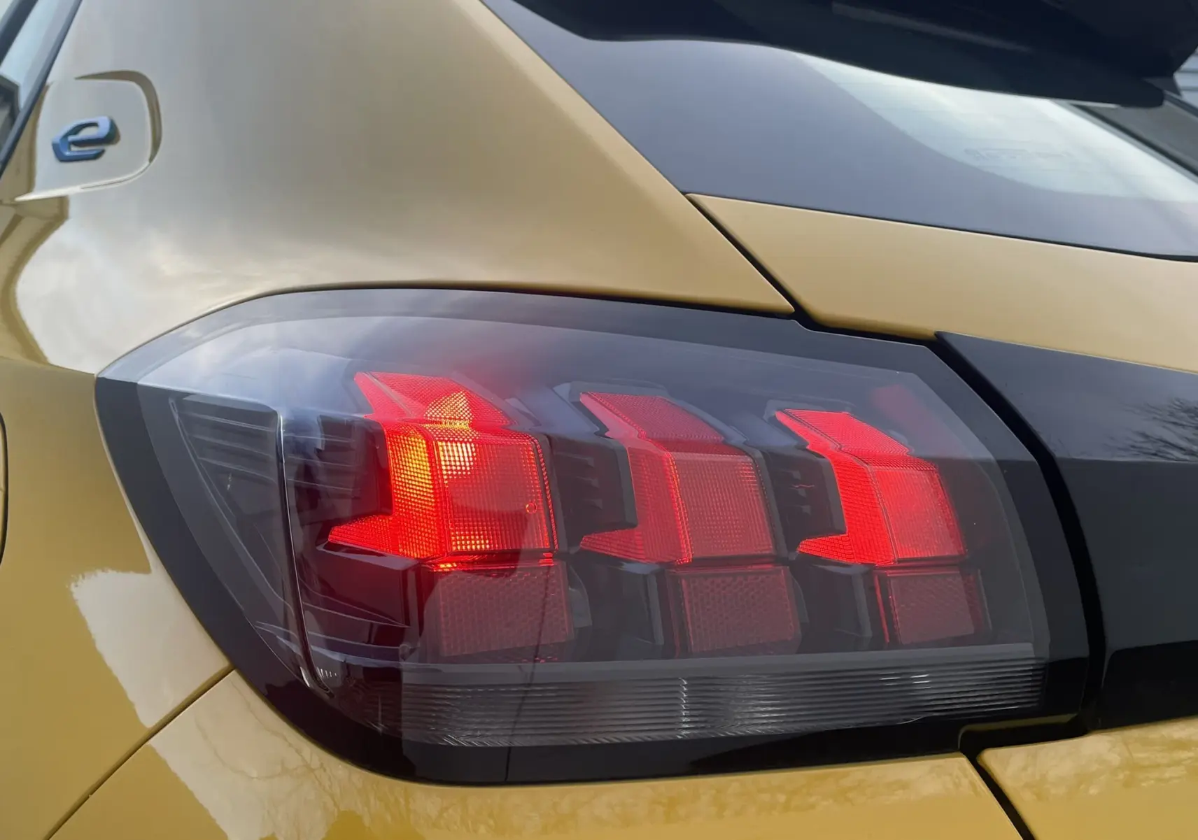 Gros plan sur le feu arrière gauche rouge d'une Peugeot 208 II électrique jaune 2023, mettant en valeur son design moderne.