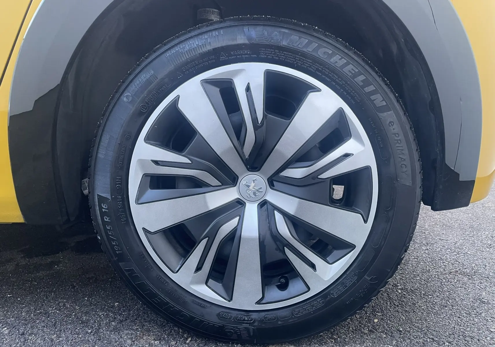 Gros plan sur la roue avant droite d'une Peugeot 208 électrique jaune 2023 avec jante alu au design moderne.