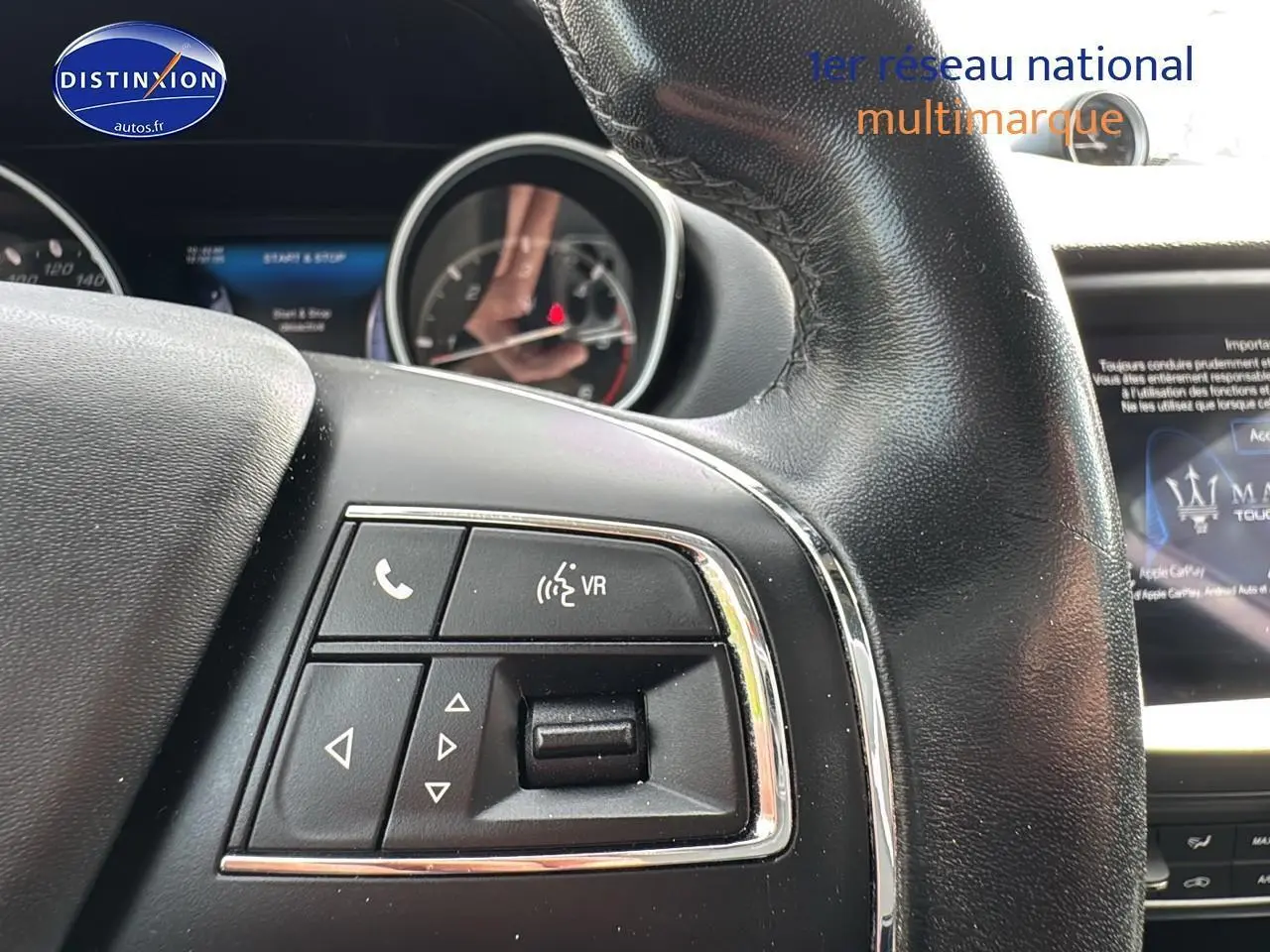 Gros plan sur les commandes vocales et multimédia du volant cuir du Maserati Levante gris, tableau de bord partiellement visible.