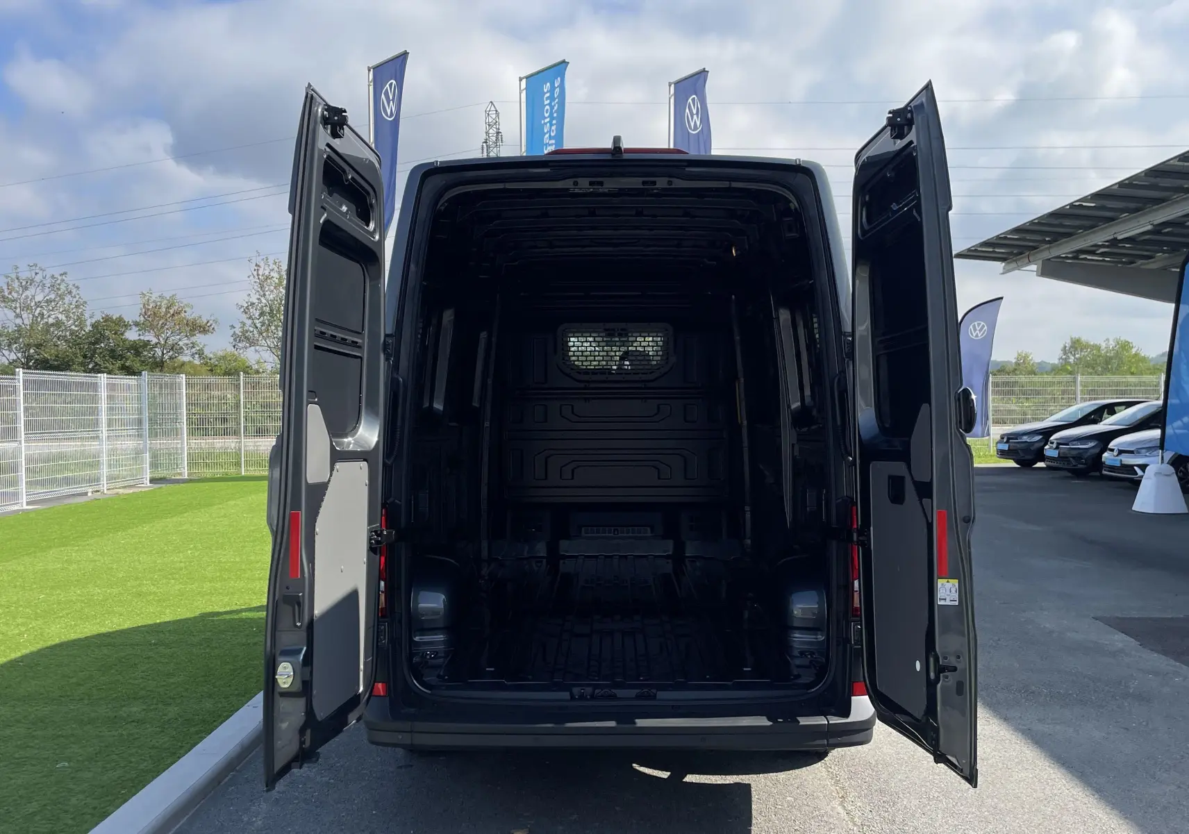 Vue arrière du Volkswagen Crafter Van gris Indium 2025 avec portes arrière ouvertes et cloison vitrée visible à l'intérieur.