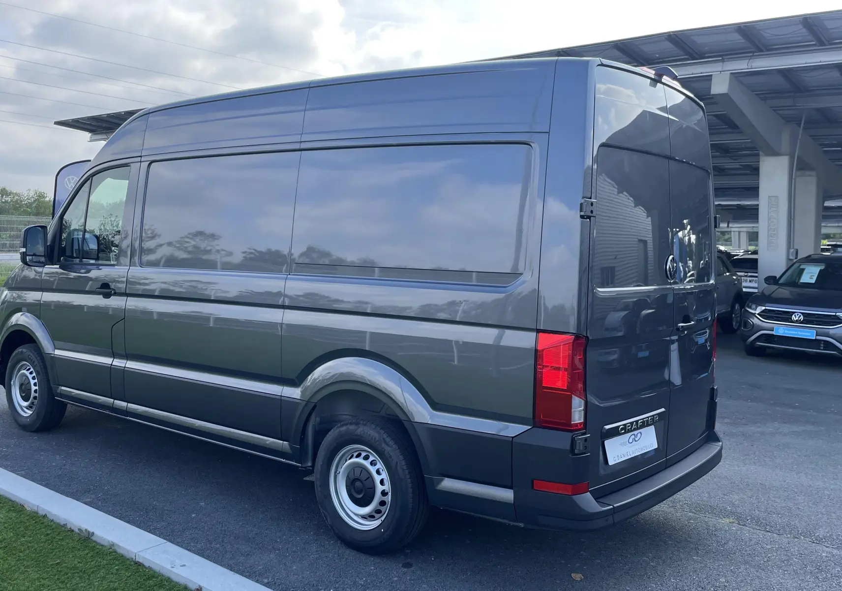 Volkswagen Crafter Van gris Indium vu en 3/4 arrière droit, avec vitres arrière teintées et feux rouges visibles.