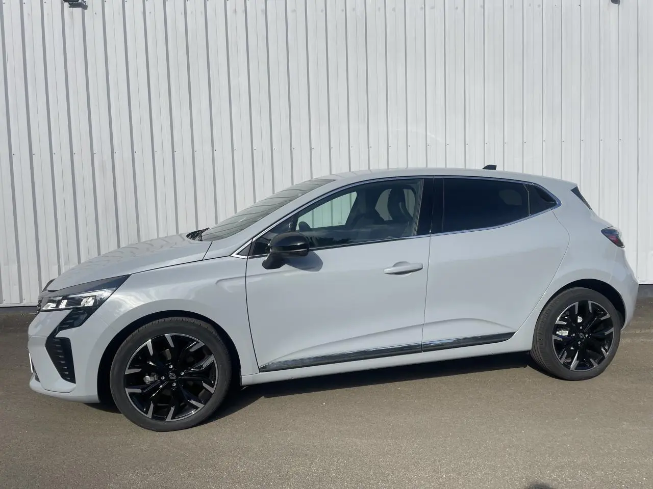 Renault Clio V TCE 90 gris Rafale vue de profil côté gauche avec jantes alliage noires et contour fenêtres aluminium.