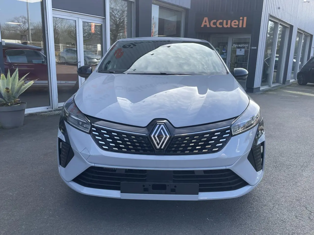 Renault Clio 2025 gris Rafale vue de face, avec calandre noire et logo Renault centré, stationnée devant un bâtiment.
