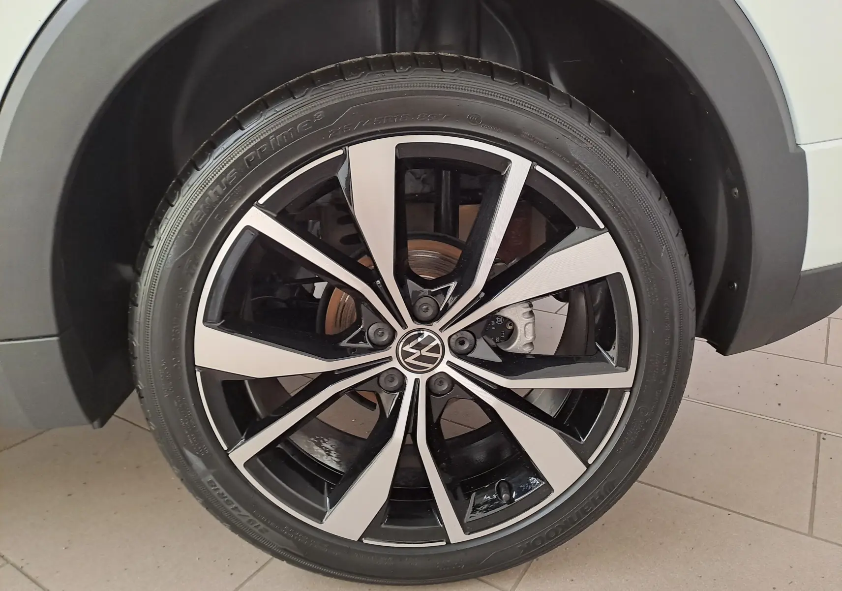 Gros plan sur la roue avant droite du Volkswagen T-Cross blanc Pur 2025, jante alliage bicolore R-Line.