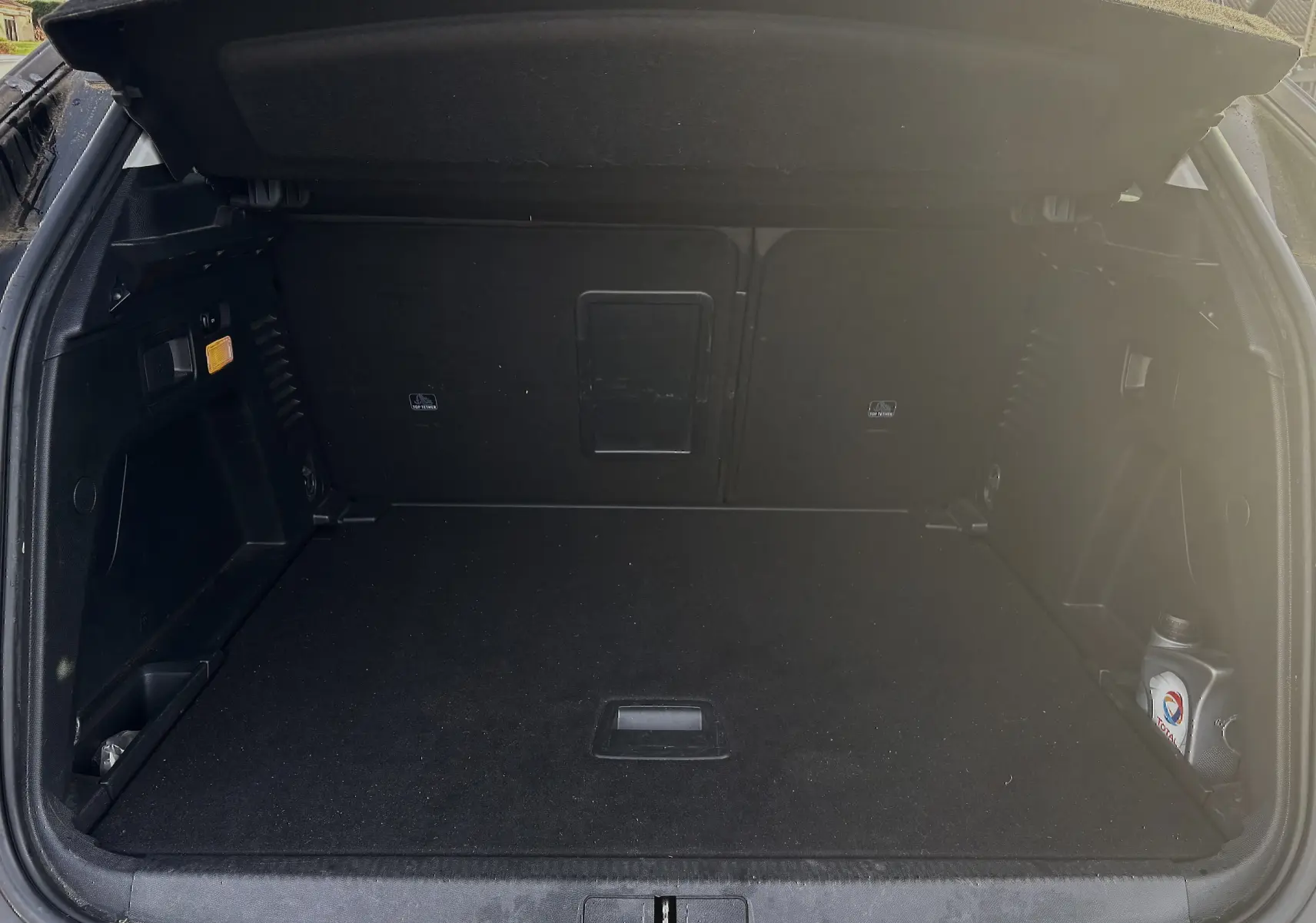 Coffre ouvert du Peugeot 3008 II diesel 2019, vue arrière, espace de chargement noir avec bouteille d'huile visible à droite.