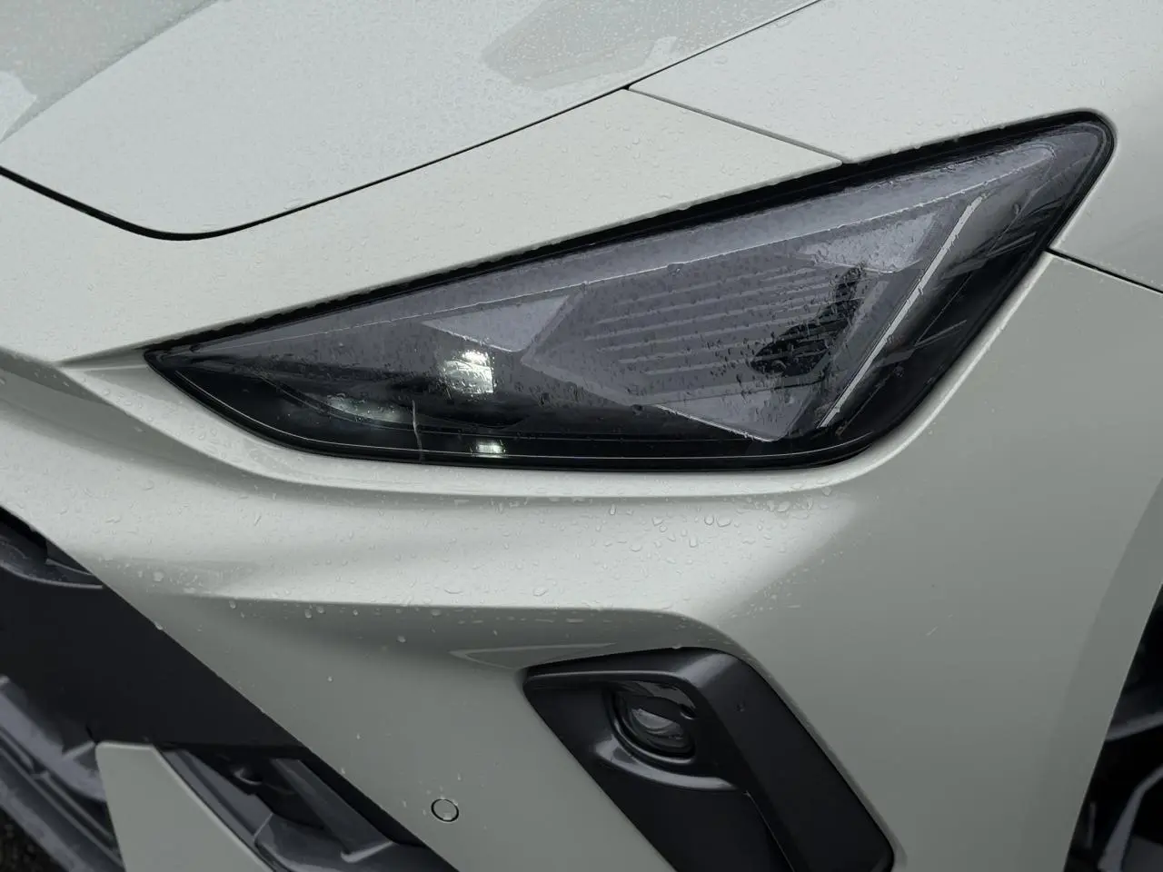 Gros plan sur le phare avant droit gris Taiga de la CUPRA LEON ST 2025 avec pluie et antibrouillard noir.