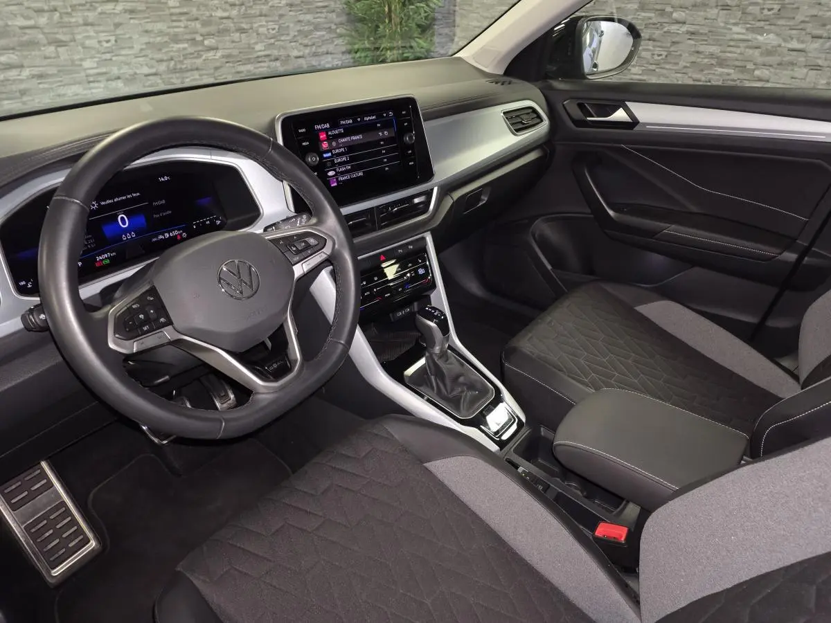 Vue intérieure côté conducteur du Volkswagen T-Roc 2025, avec tableau de bord digital et sellerie tissu noir et gris.