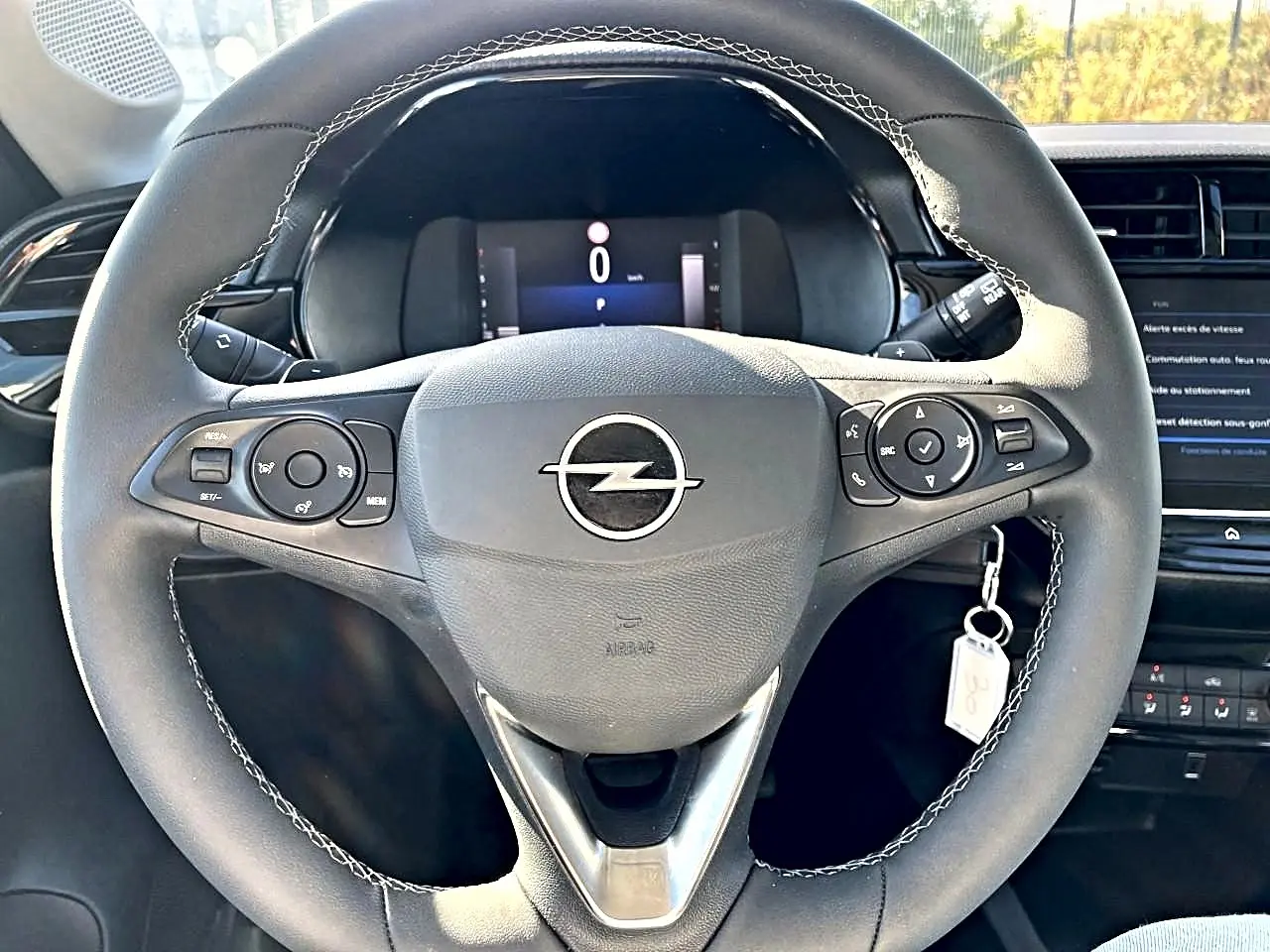 Vue frontale du volant sport noir avec surpiqûres blanches et logo Opel au centre du tableau de bord gris.