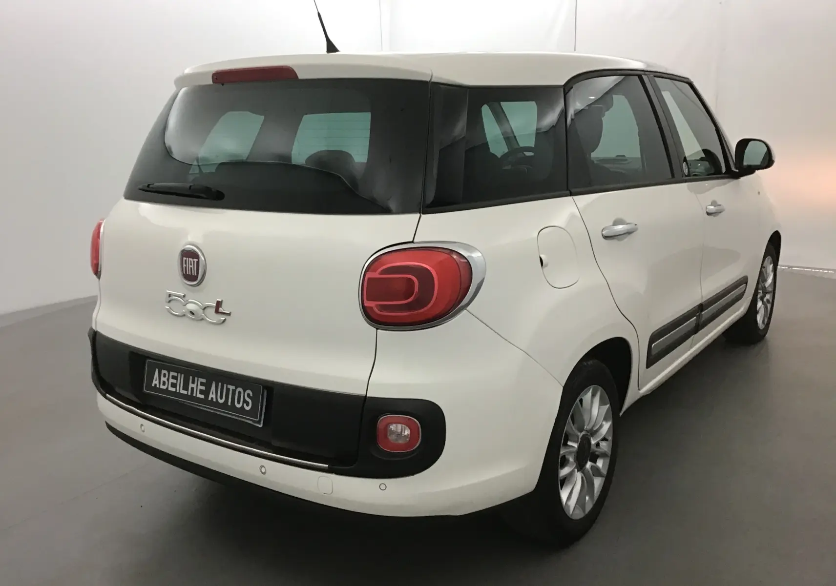 Vue 3/4 arrière droite d'une Fiat 500L blanche avec lunette arrière surteintée et feux arrière caractéristiques.