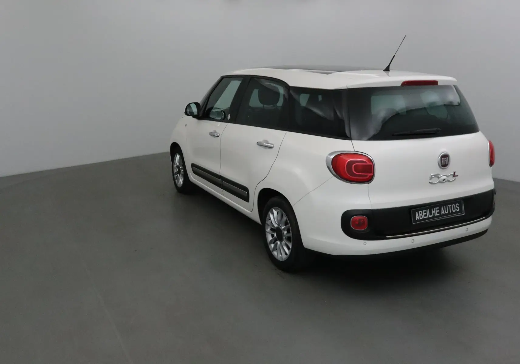 Fiat 500L blanc vue 3/4 arrière droit, avec lunette arrière surteintée et feux arrière arrondis distinctifs.