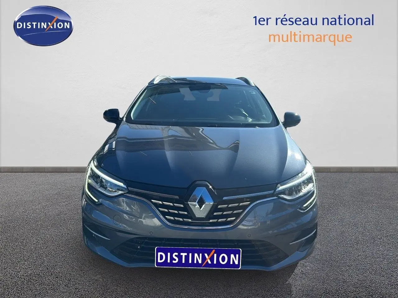 Vue frontale d'une Renault Mégane Break gris titanium métal avec calandre chromée et phares LED allumés.