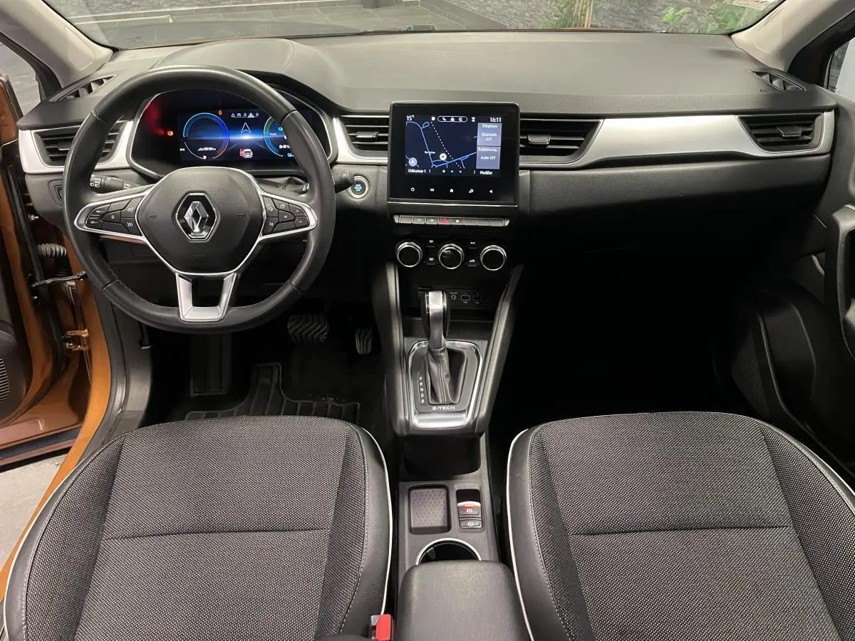 Vue intérieure avant du Renault Captur orange 2022, tableau de bord moderne avec écran tactile et volant multifonction noir.