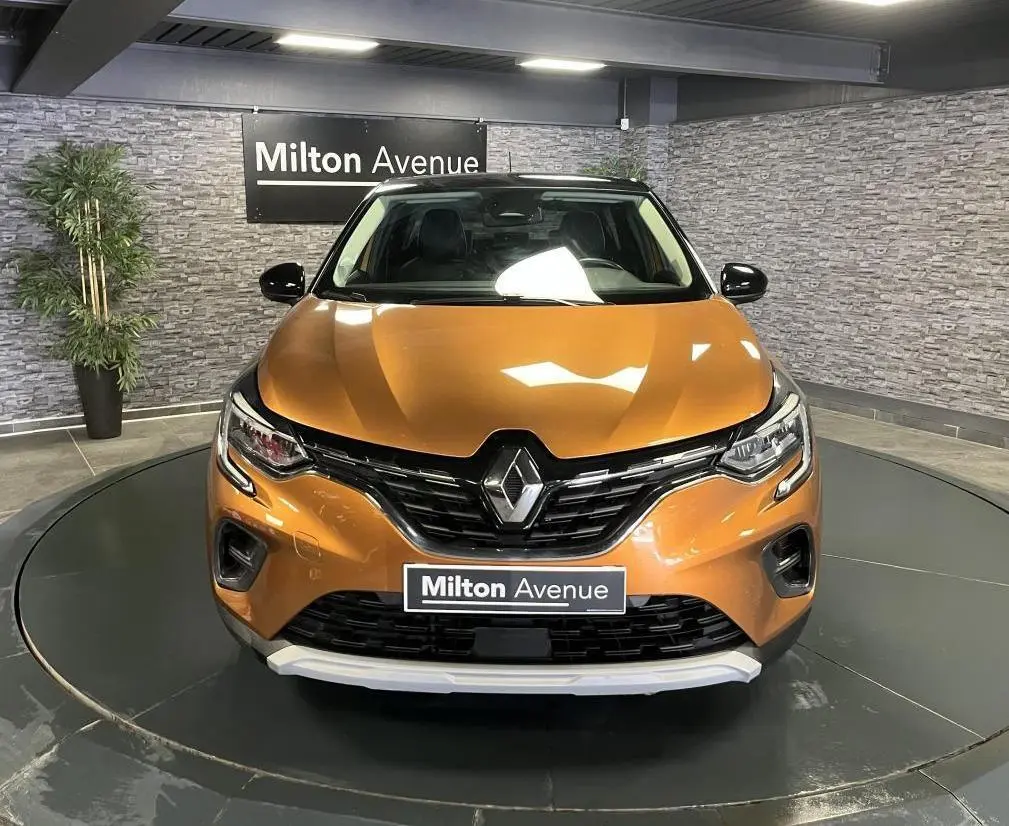 Vue frontale d'un Renault Captur orange avec calandre noire et détails chromés, en intérieur showroom.