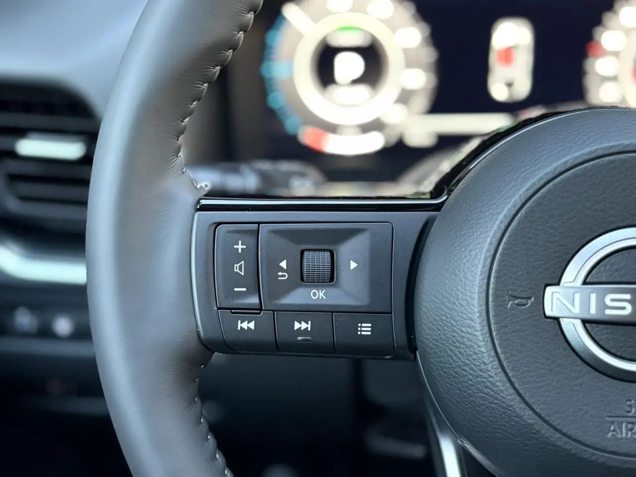 Gros plan sur les commandes au volant côté gauche du Nissan Qashqai 2025, volant cuir noir avec logo Nissan visible.