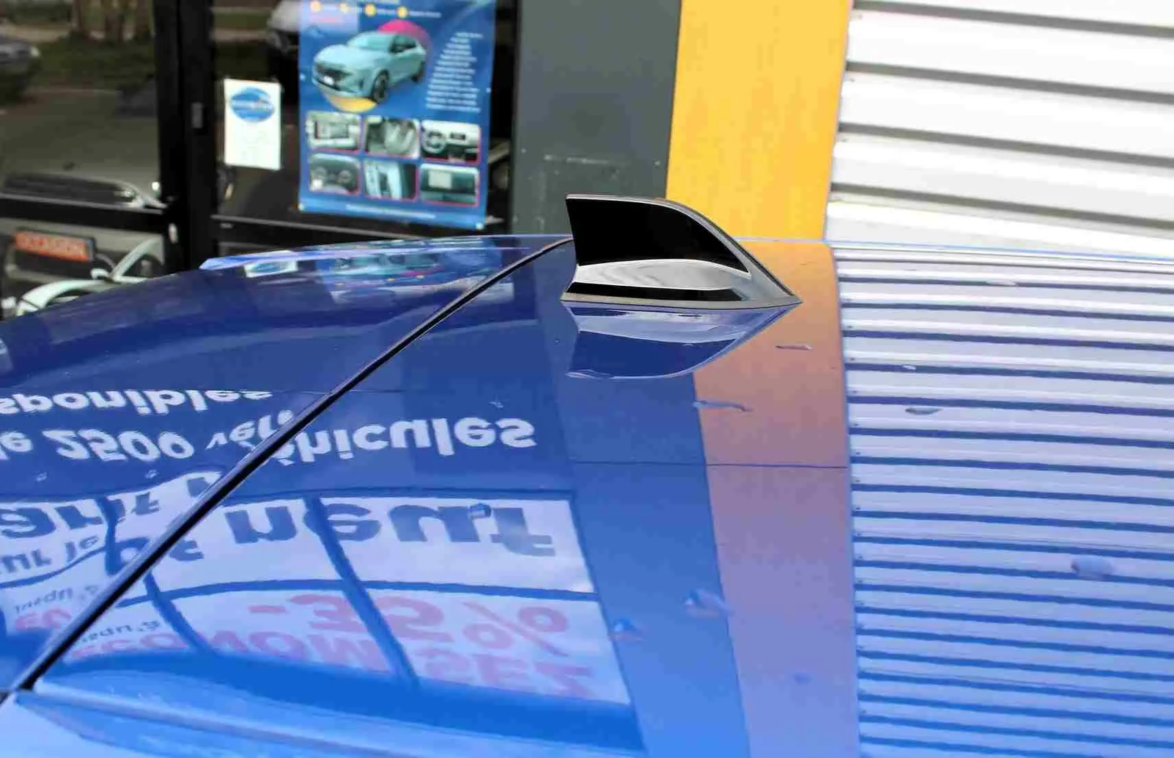 Gros plan sur l'antenne requin sur le toit bleu iron metal d'une Renault Symbioz 2025, reflet d'une enseigne visible.