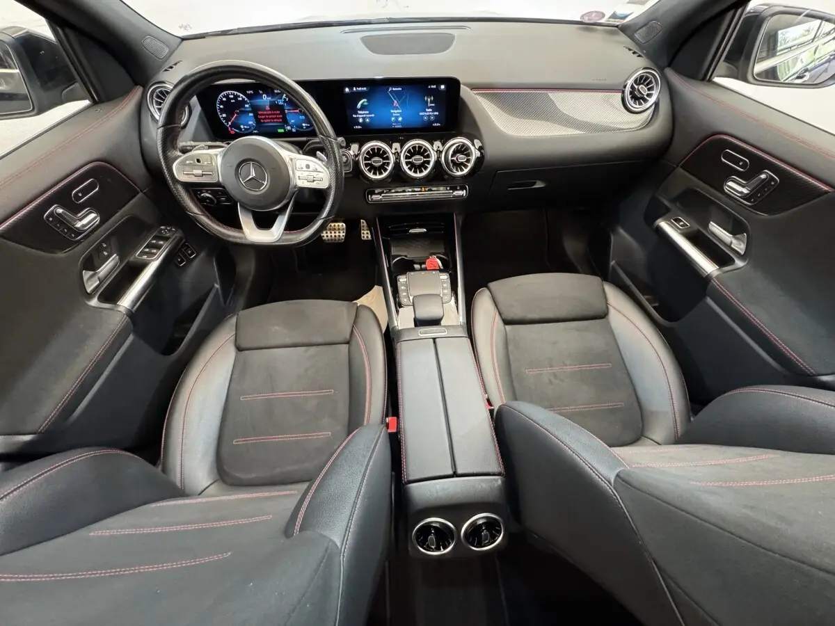 Vue intérieure avant de la Mercedes GLA 250 e AMG Line 2021, avec tableau de bord numérique et sièges noirs à surpiqûres rouges.