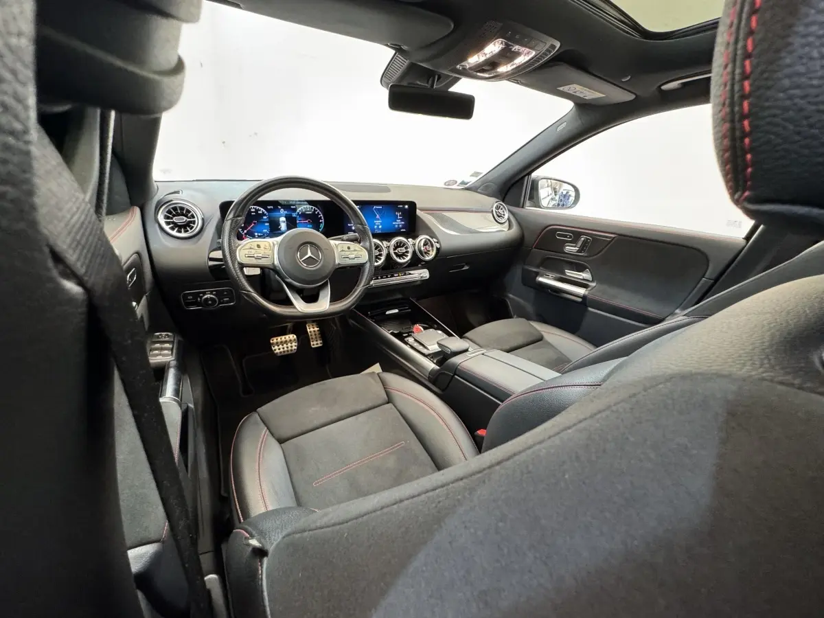 Vue intérieure avant droite de la Mercedes GLA 250 e AMG Line 2021, sièges noirs avec surpiqûres rouges et tableau de bord numérique.