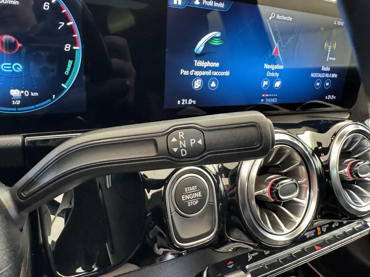 Gros plan intérieur sur la commande de boîte auto et le bouton Start Engine, avec écran tactile et aérateurs ronds chromés.
