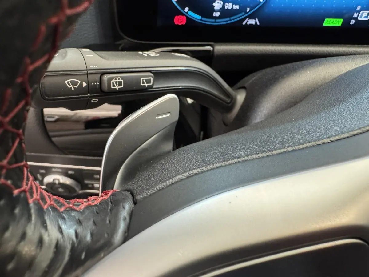 Gros plan sur la palette de changement de vitesse derrière le volant cuir noir avec surpiqûres rouges d'une Mercedes GLA 250 e AMG Line 2021.