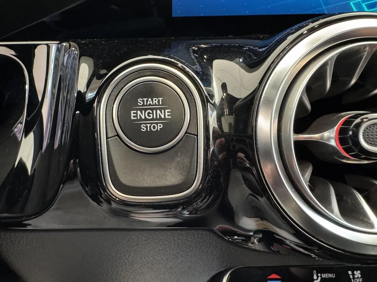 Gros plan sur le bouton start/stop moteur noir brillant et la sortie d'air circulaire chromée du tableau de bord Mercedes GLA 250 e AMG Line.