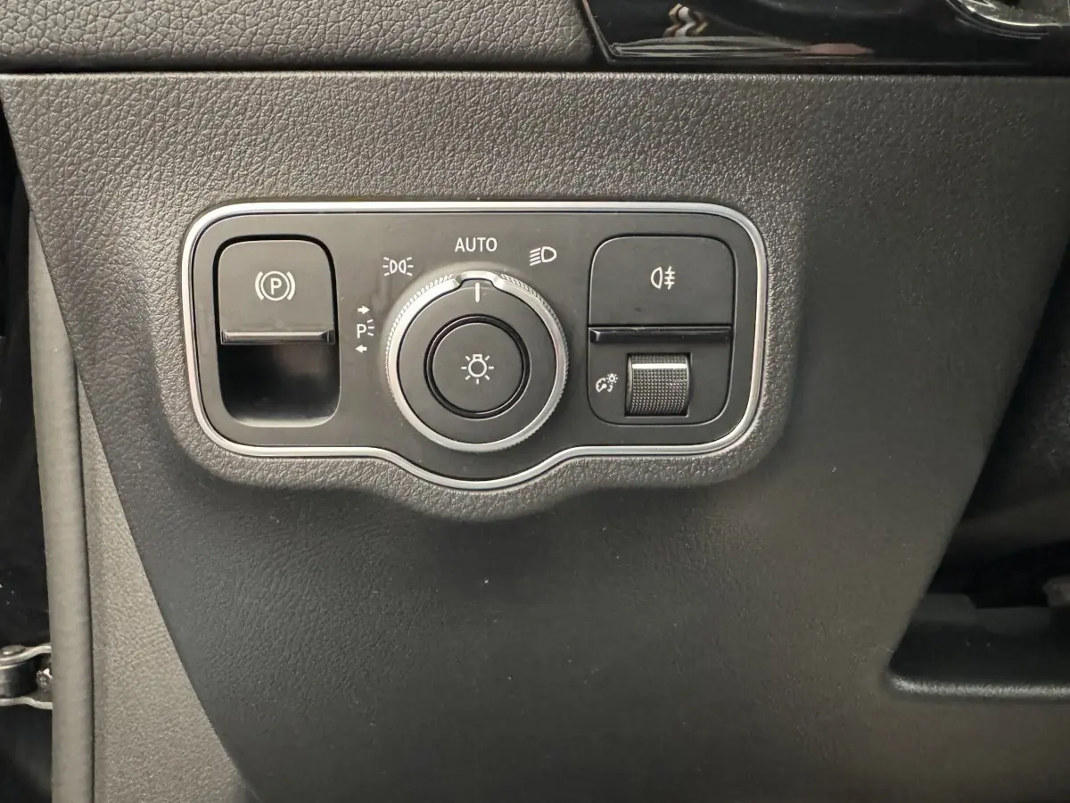 Gros plan sur le panneau de commande des phares et du frein à main électrique dans une Mercedes GLA 250 e AMG Line noire.