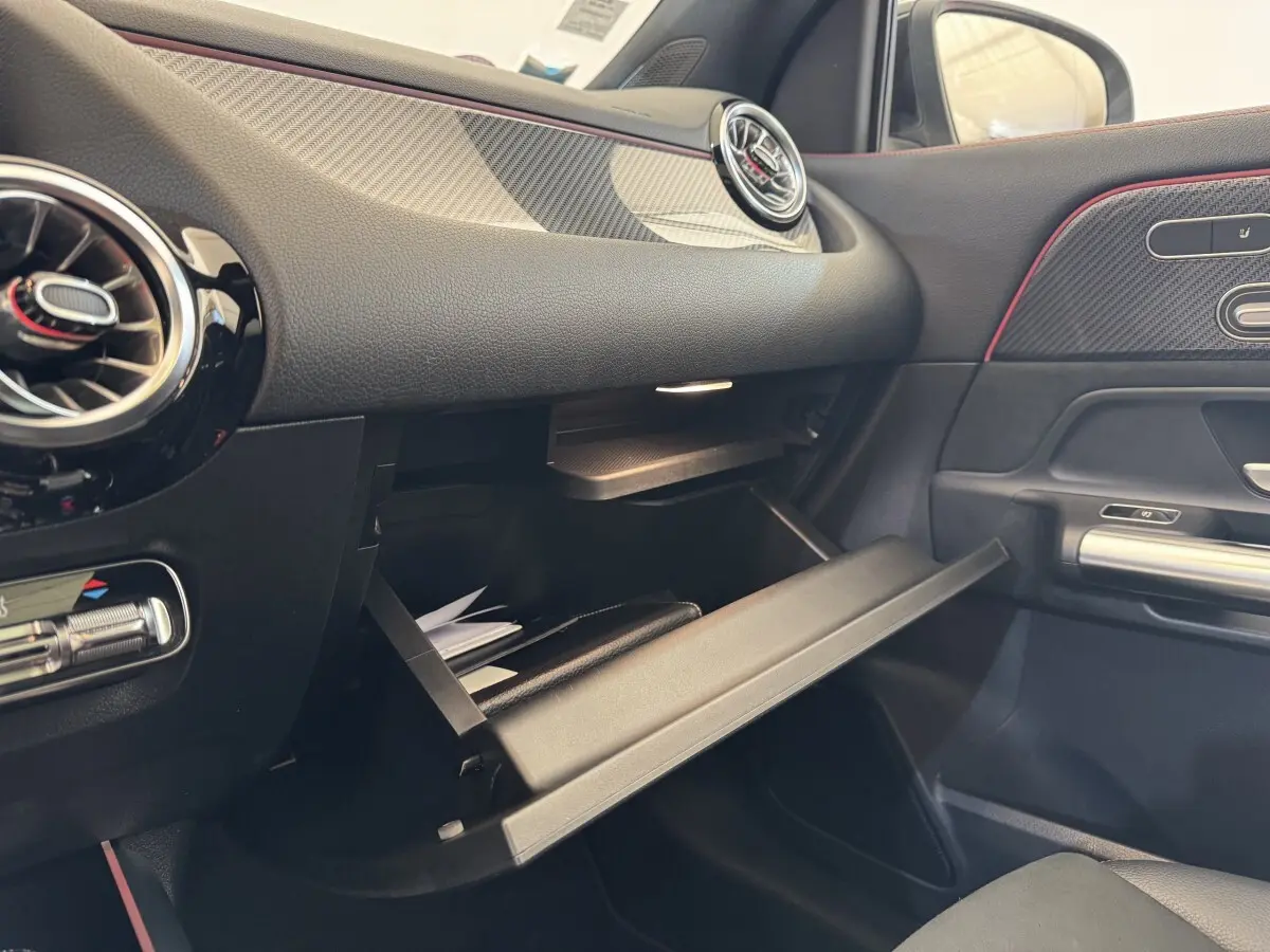 Vue intérieure côté passager du tableau de bord noir avec boîte à gants ouverte et aérateurs ronds du Mercedes GLA 250 e AMG Line.