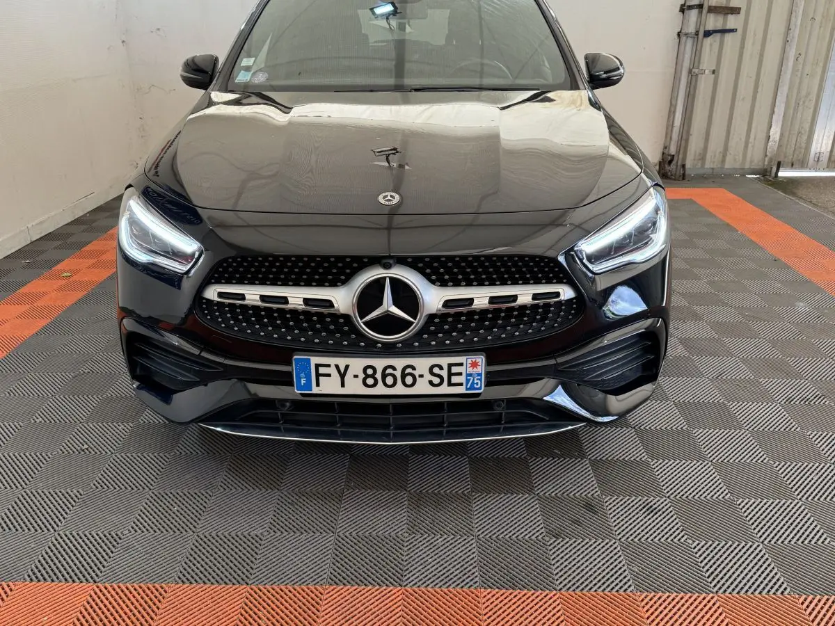 Vue avant d'une Mercedes GLA 250 e AMG Line noire, avec calandre étoilée et phares LED allumés dans un garage.