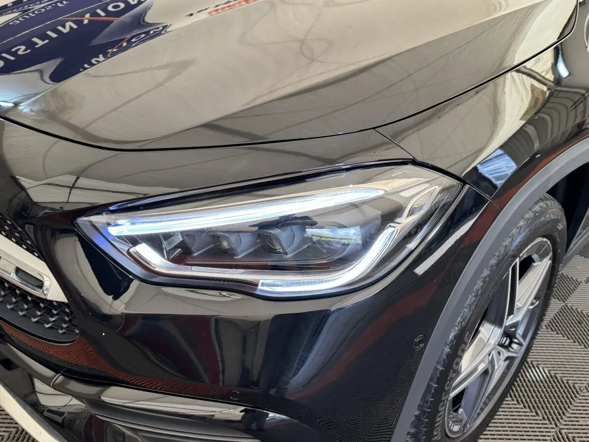 Gros plan sur le phare avant droit et la roue d’une Mercedes GLA 250 e AMG Line noire, finition brillante.