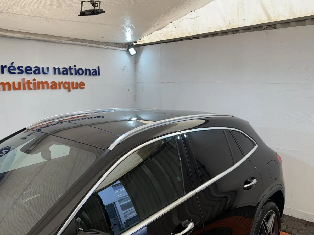 Vue 3/4 arrière droite d’un Mercedes GLA 250 e AMG Line noir avec vitres teintées et barres de toit chromées dans un showroom.