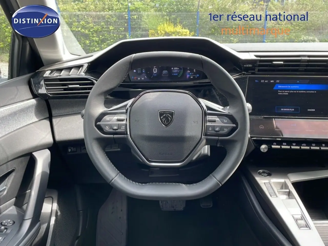 Vue intérieure centrée sur le volant noir de la Peugeot 308 SW Hybrid 2025 avec tableau de bord digital et console moderne.