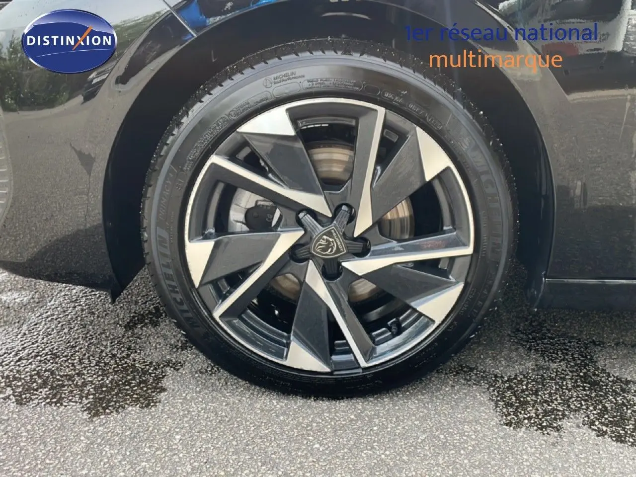 Gros plan sur la roue avant gauche d’une Peugeot 308 SW Hybrid noire métal avec jante alliage bicolore distinctive.