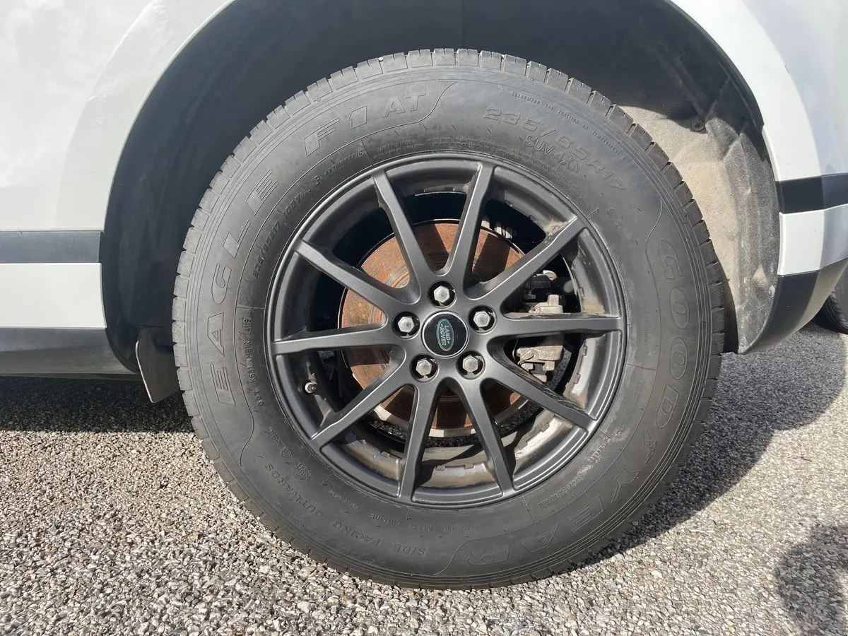 Gros plan sur la roue avant droite d'un Range Rover Evoque blanc 2020 avec jante noire et logo Land Rover central.