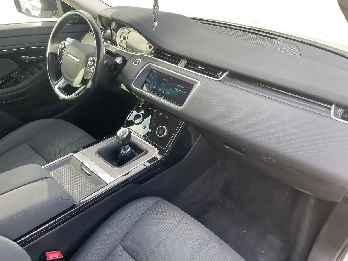 Vue intérieure côté conducteur du Range Rover Evoque 2020 blanc, mettant en valeur la console centrale avec boîte manuelle et écran tactile.