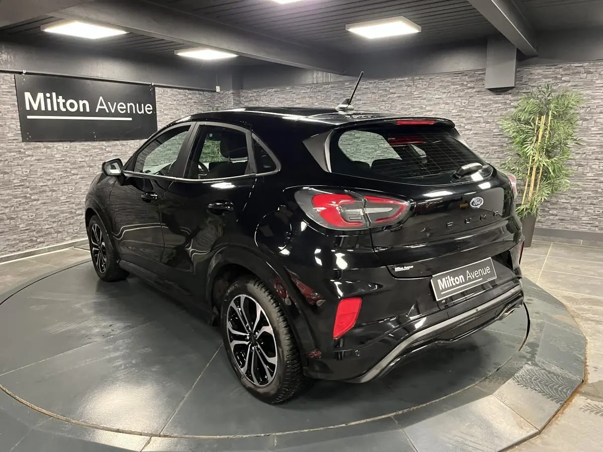 Vue 3/4 arrière droite du Ford Puma noir métallisé avec jantes alliage 17'' et badges ST-Line dans un showroom.