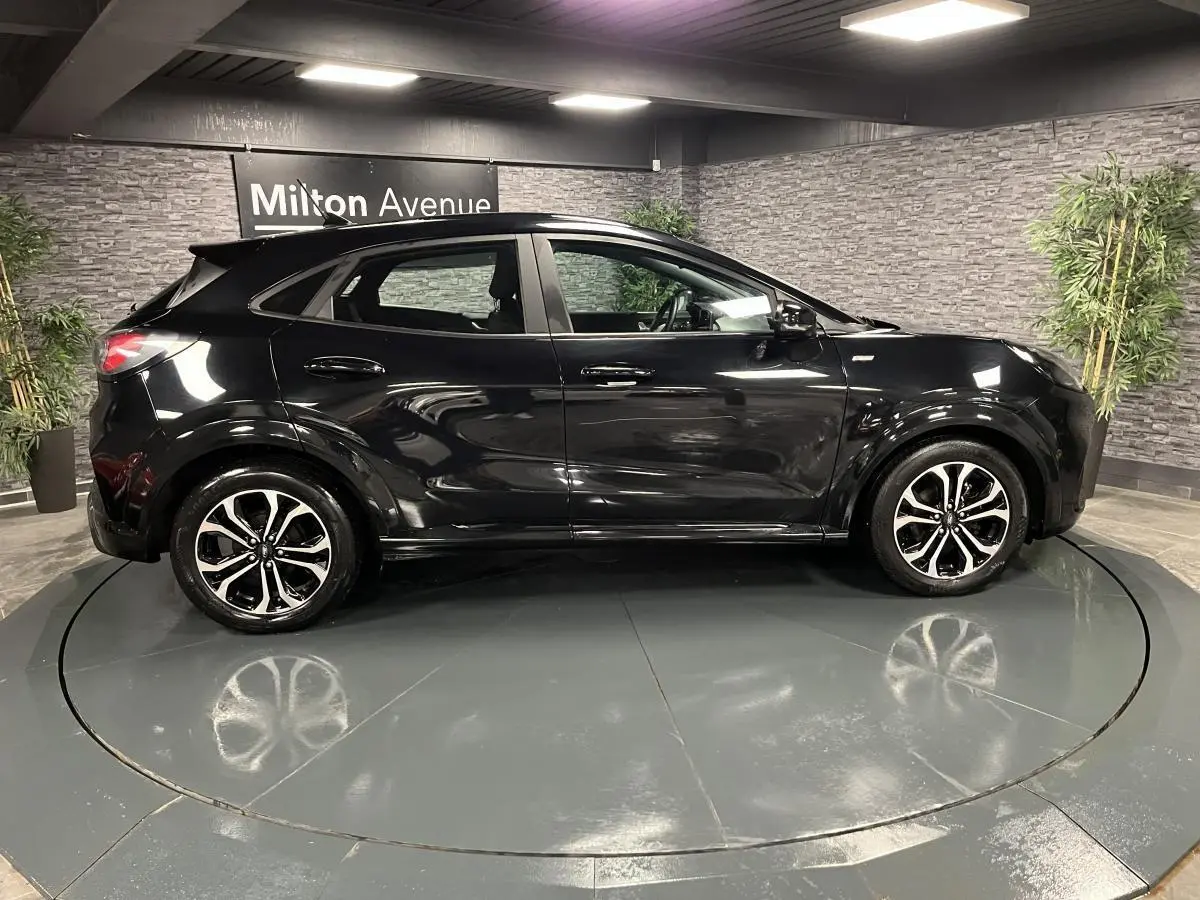 Ford Puma noir vue de profil côté gauche, avec jantes alliage noires et détails brillants en intérieur showroom.