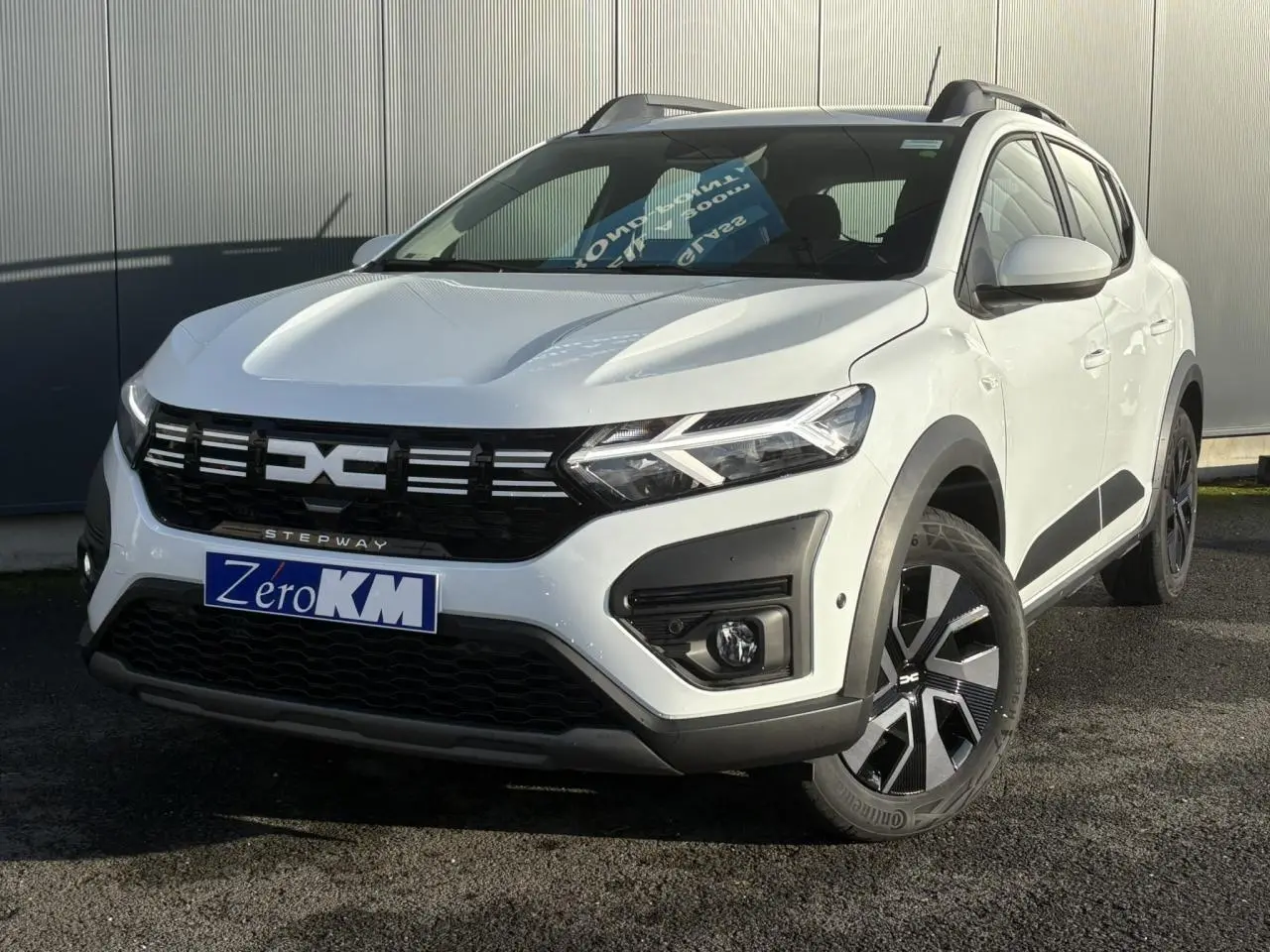 Vue 3/4 avant droite d'une Dacia Sandero Stepway blanche Glacier avec signature lumineuse LED et jantes noires distinctives.