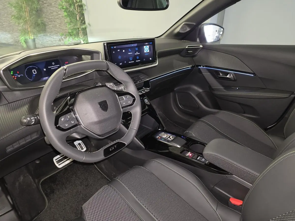Intérieur avant droit de la Peugeot 208 GT 2025 avec volant cuir, écran tactile et sellerie tissu noire.