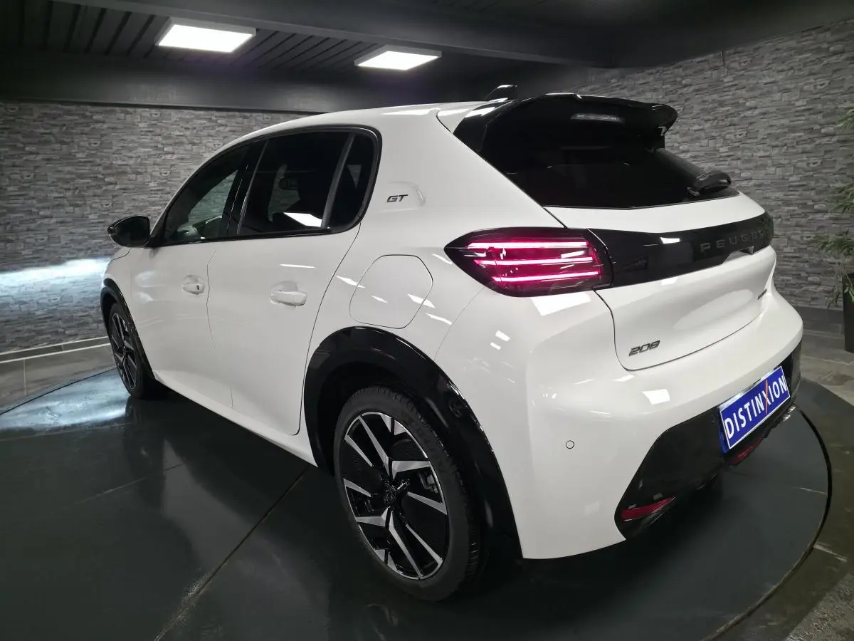 Vue 3/4 arrière droite d'une Peugeot 208 GT blanche avec jantes alliage bi-ton et feux arrière LED allumés.