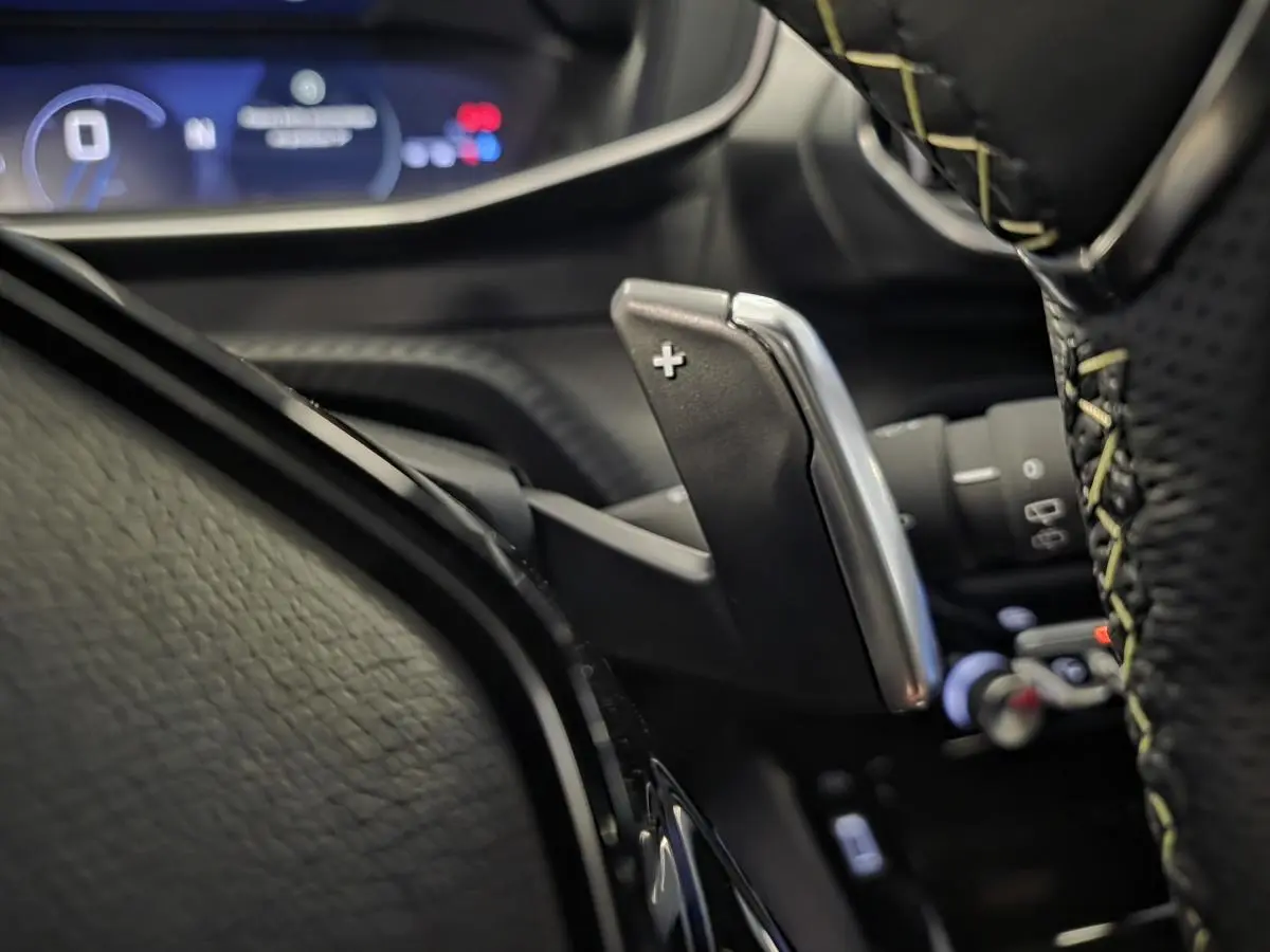 Gros plan sur la palette de changement de vitesse droite en aluminium et volant cuir perforé avec surpiqûres vertes Peugeot 208 GT.