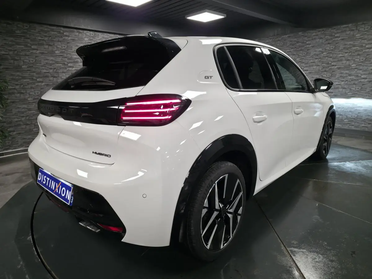 Vue 3/4 arrière droite d'une Peugeot 208 blanche hybride avec jantes alliage bi-tons et feux arrière LED distinctifs.