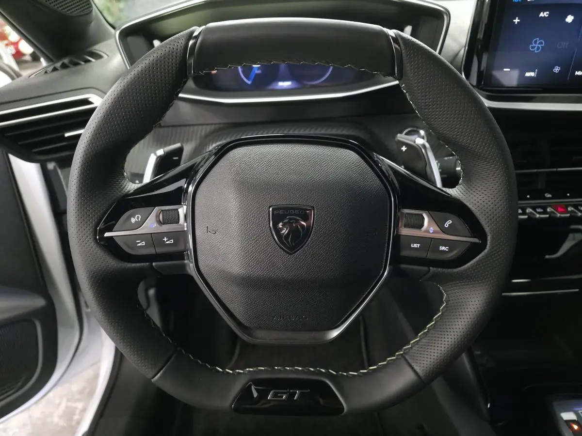 Volant cuir noir perforé avec badge GT au centre, vue rapprochée de l’habitacle de la Peugeot 208 blanche 2025.